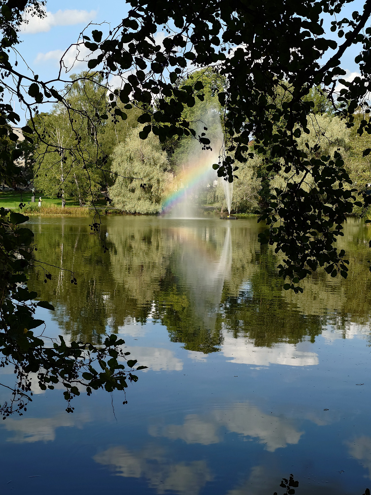 池の噴水と虹が綺麗に映る公園の風景